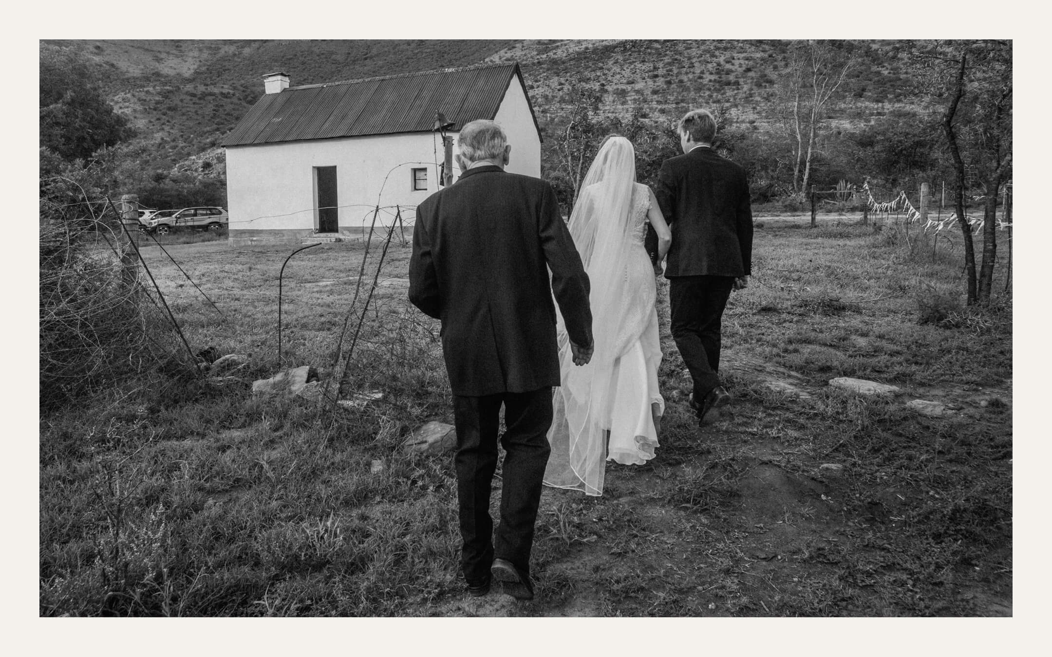 Bride walking to a small country chapel between her father and another man. Ben Viljoen Photography