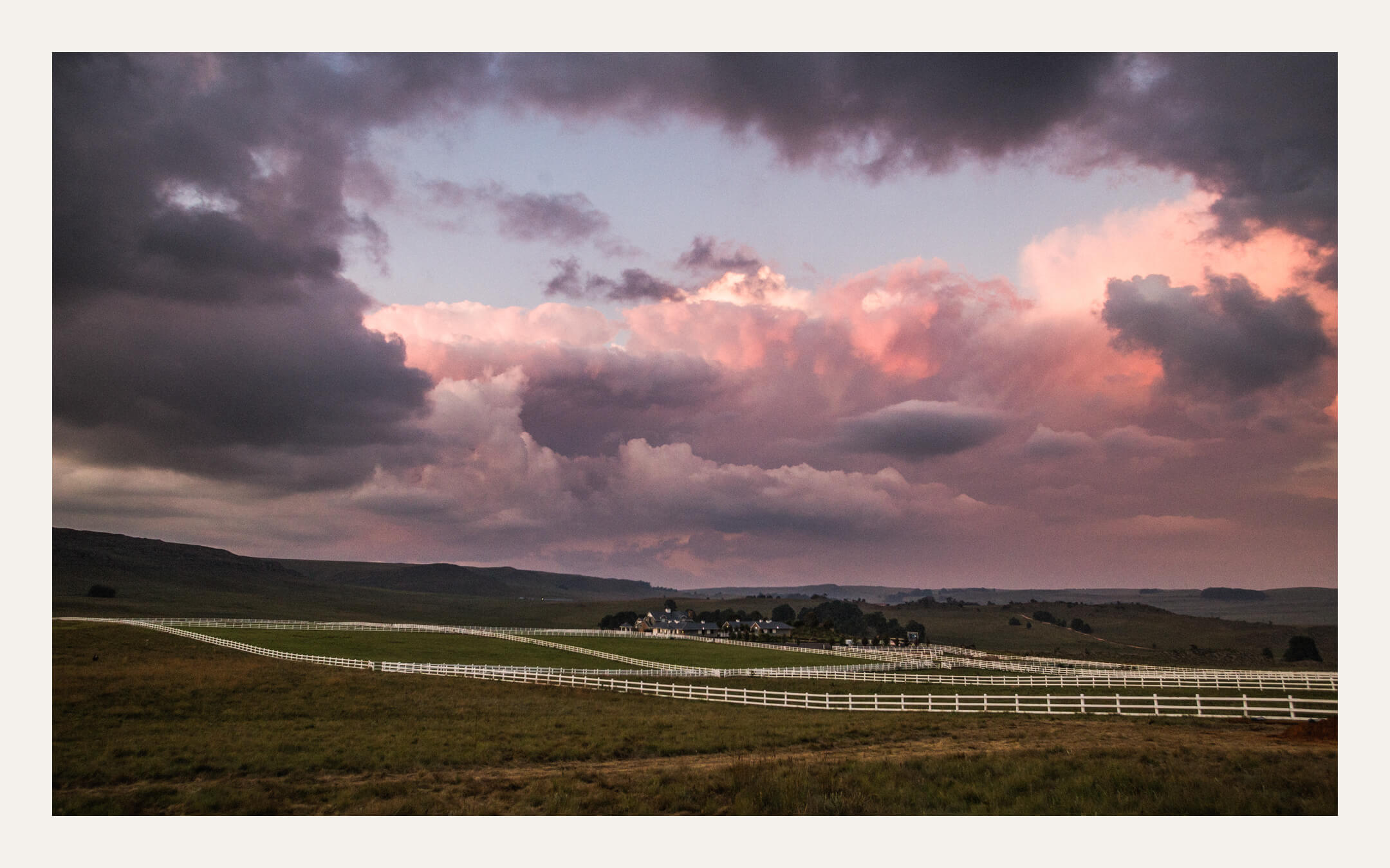 Wide sunset over farmland with a pink storm cloud above the hills. Ben Viljoen Photography