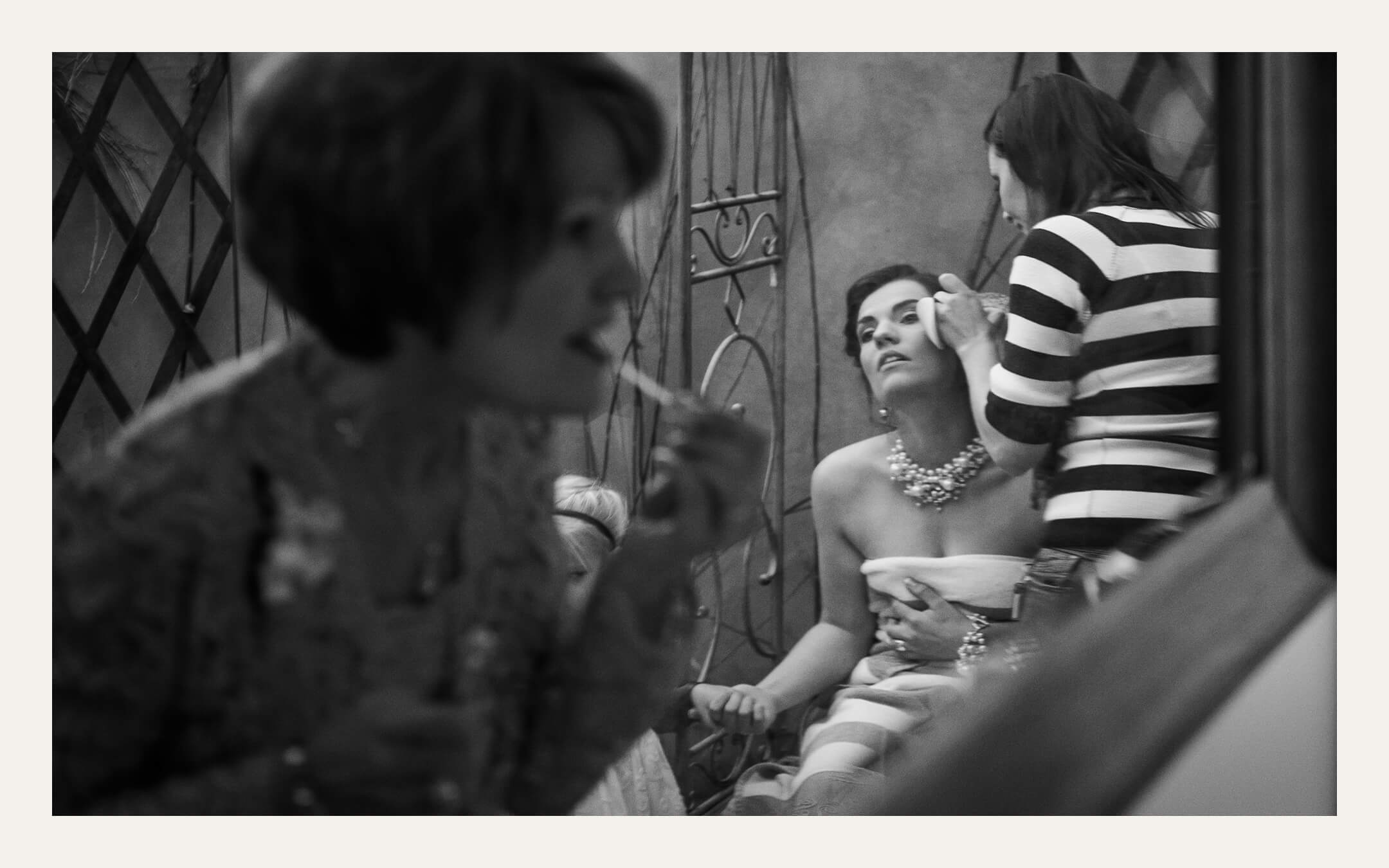 Bride having makeup done, reflected in a mirror with a guest in the foreground. Ben Viljoen Photography