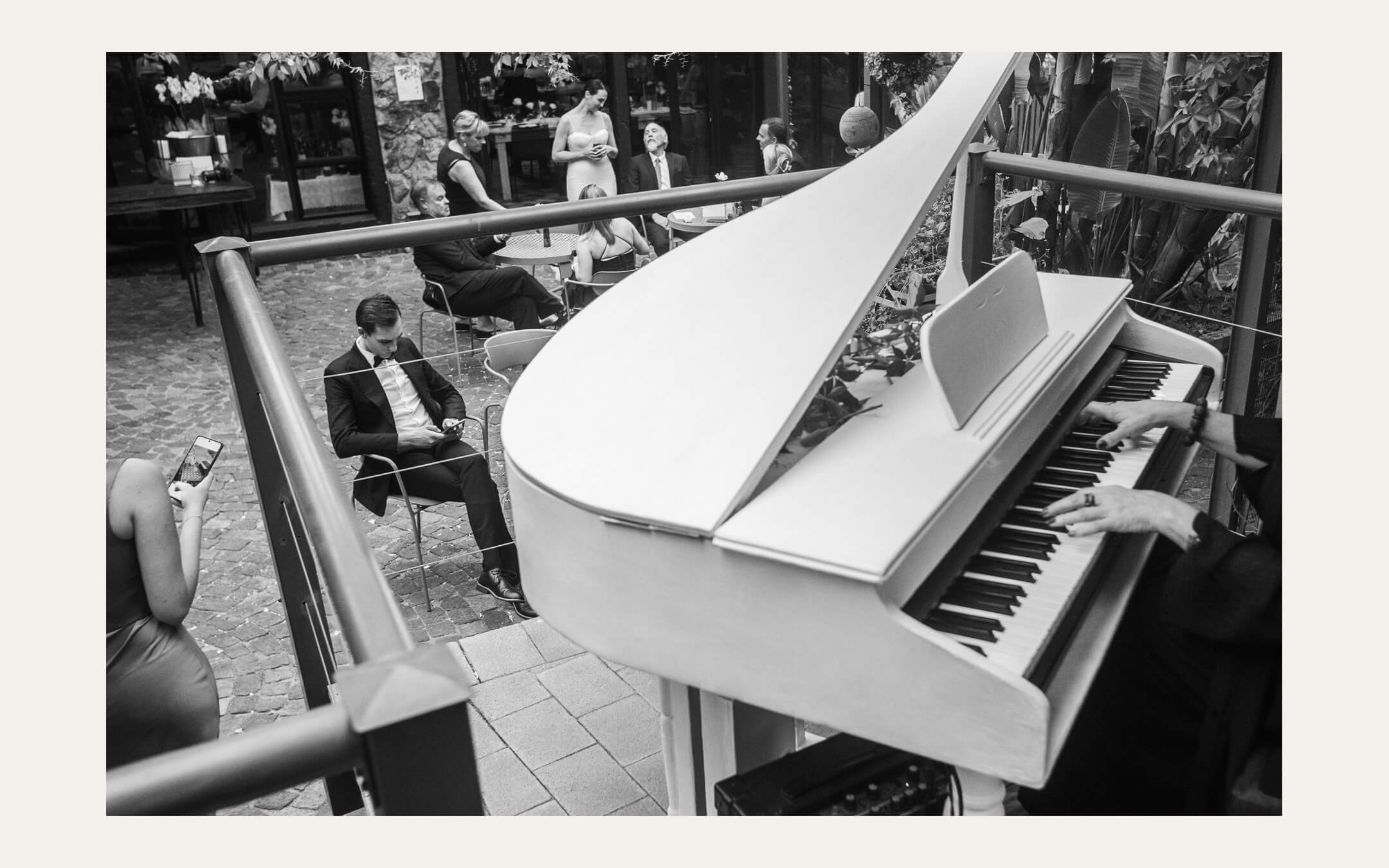 Pianist playing a white grand piano as guests sit in the courtyard behind. Ben Viljoen Photography