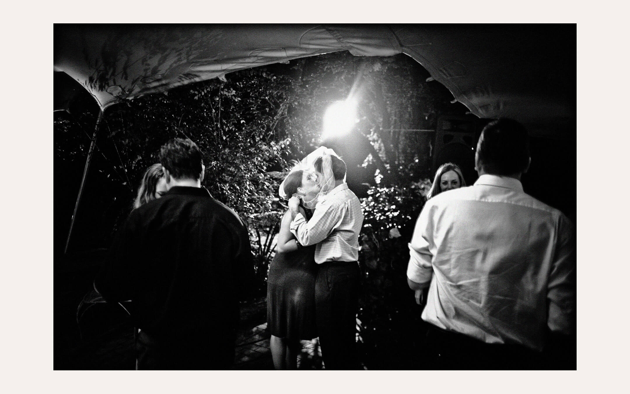 Couple kissing under a lit marquee in the rain. Ben Viljoen Photography